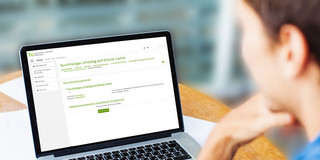 Studierende sitzt am Arbeitsplatz und schaut auf den Laptop.
